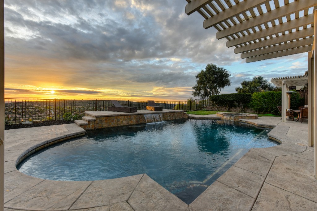Custom pool with stone waterfall feature at sunset overlooking a valley