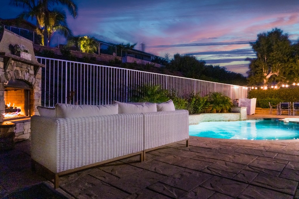 Twilight backyard with illuminated pool, stone fireplace, and string lights